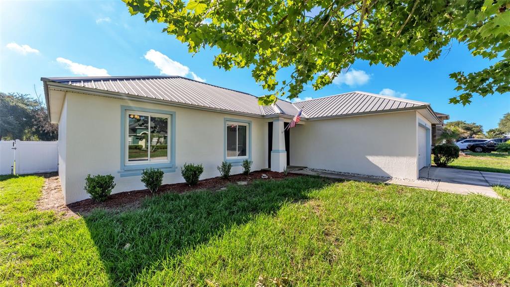 A single-story house with a light-colored exterior, metal roof, and a small front yard — 5576 MOON VALLEY DRIVE, LAKELAND, FL