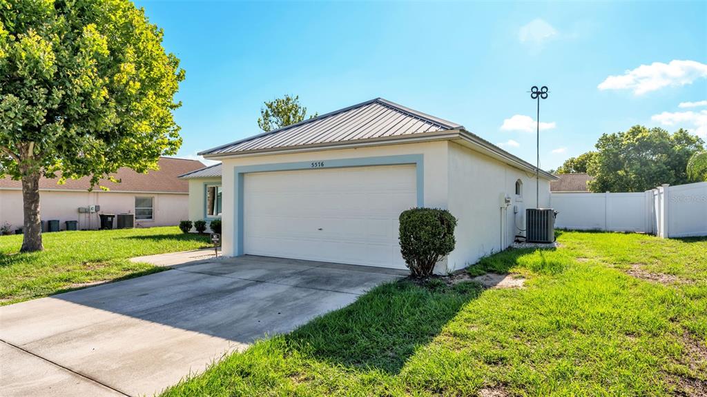 A single-story house with a white garage door, metal roof, and a concrete driveway — 5576 MOON VALLEY DRIVE, LAKELAND, FL