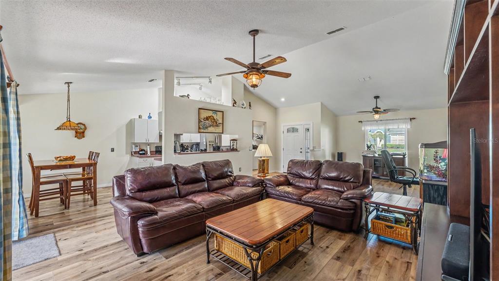 A living room with wood-look flooring, leather sofas, and a vaulted ceiling with ceiling fans — 5576 MOON VALLEY DRIVE, LAKELAND, FL