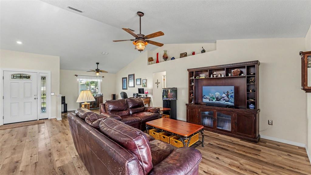 A living room features wood-look flooring, a vaulted ceiling, leather sofas, and a large entertainment center — 5576 MOON VALLEY DRIVE, LAKELAND, FL