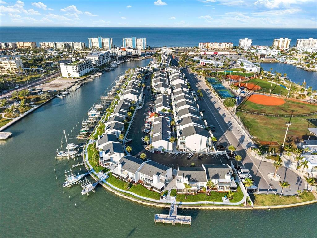 An aerial view shows a waterfront townhouse complex with boat slips and adjacent sports fields — 337 REX PLACE UNIT A, MADEIRA BEACH, FL