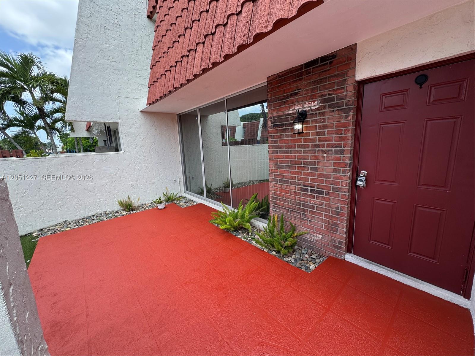 A red-tiled patio leads to a red front door and a brick-accented exterior wall — MIAMI, FL