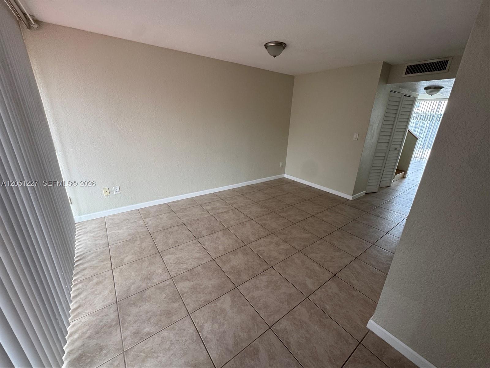 An empty room features beige walls, large square floor tiles, and a sliding glass door — MIAMI, FL