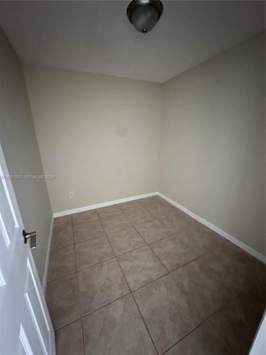 A small, empty room features beige walls, a ceiling light fixture, and tiled flooring — MIAMI, FL