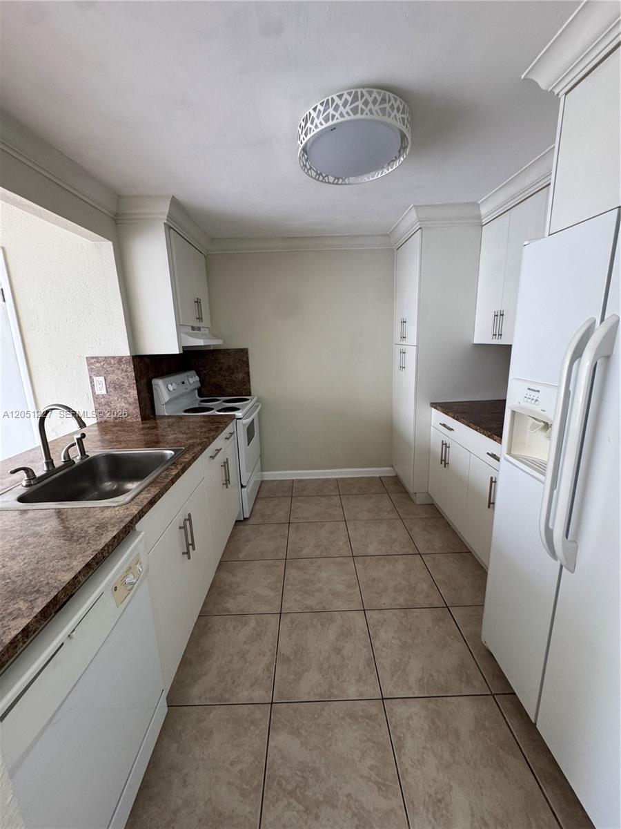 A galley kitchen features white cabinets, brown laminate countertops, tile flooring, and white appliances — MIAMI, FL