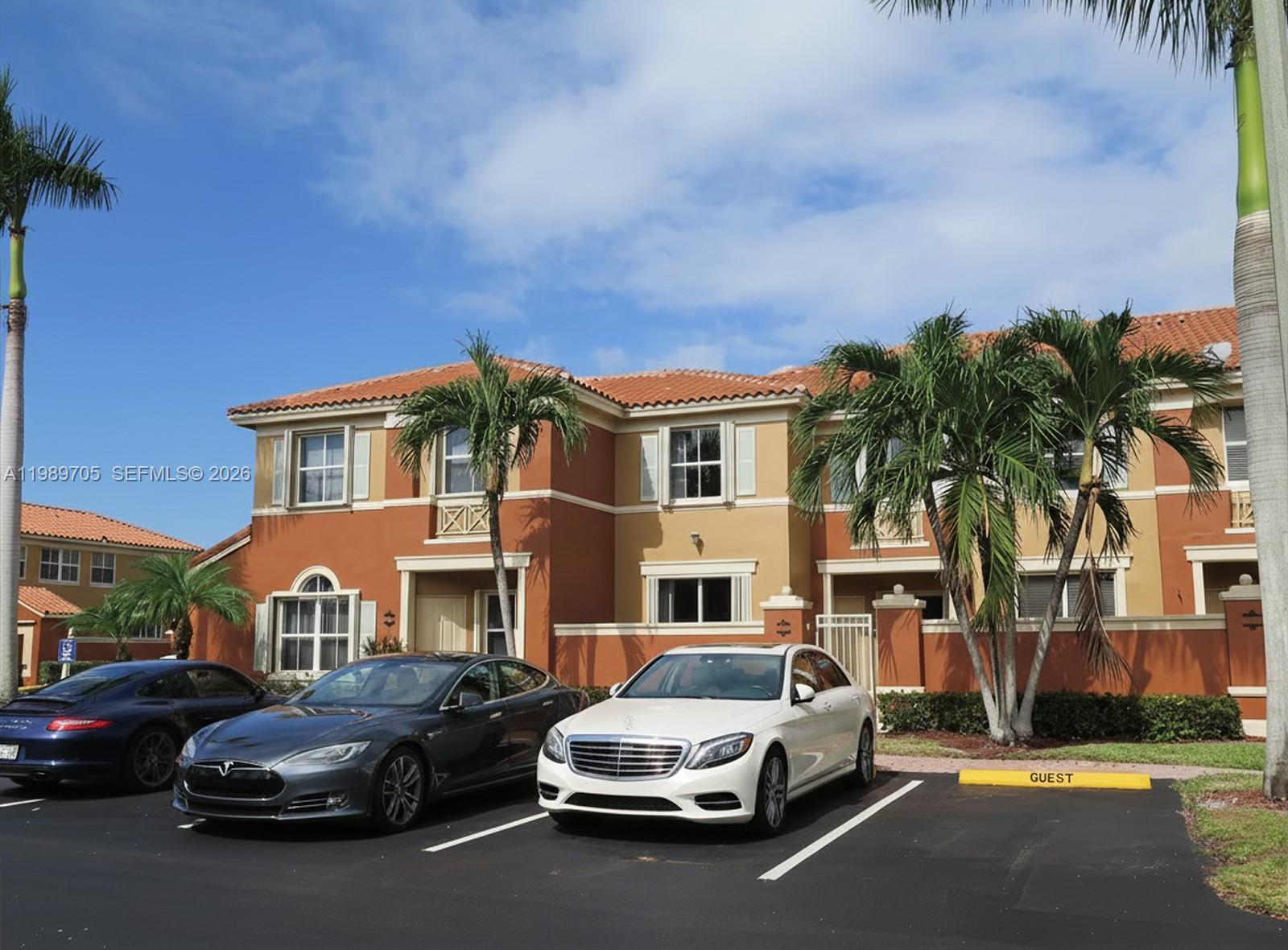 A two-story townhouse with orange and tan stucco walls sits behind a parking lot — 11479 NW 60th Ter # 373, Doral FL 33178, DORAL, FL