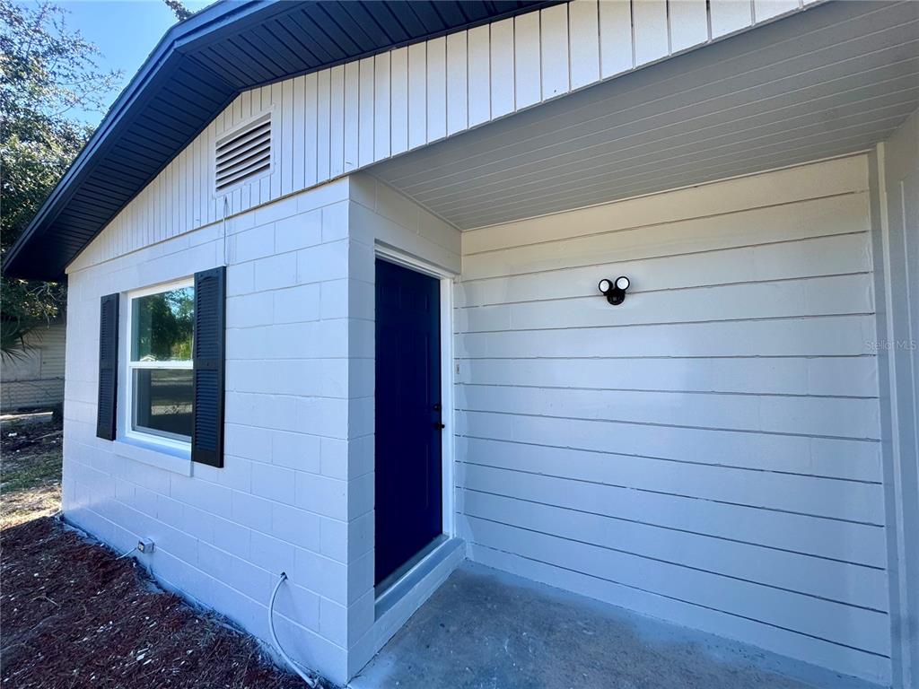 A white concrete block house exterior features a dark blue door and a small porch — 7224 VALIANT COURT, ORLANDO, FL