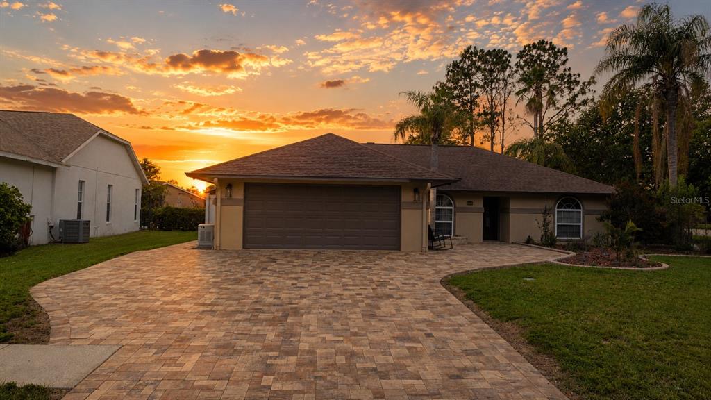 A single-story house with a paved driveway and garage at sunset — 6441 SILVER OAKS DRIVE, ZEPHYRHILLS, FL
