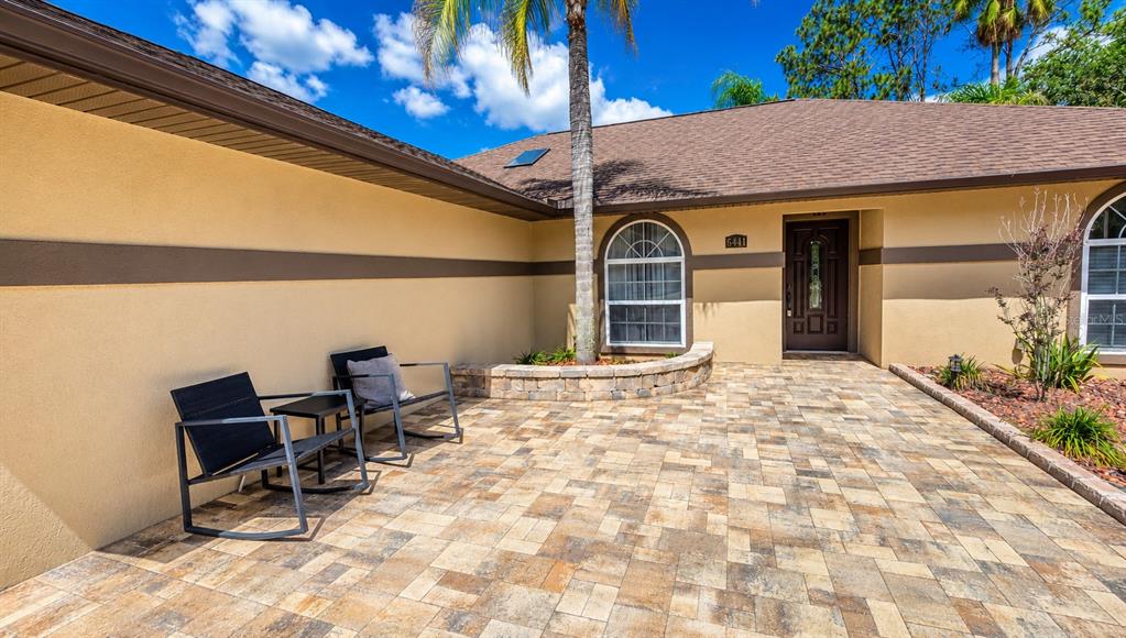 A paved patio sits in front of a house with a brown door and windows — 6441 SILVER OAKS DRIVE, ZEPHYRHILLS, FL