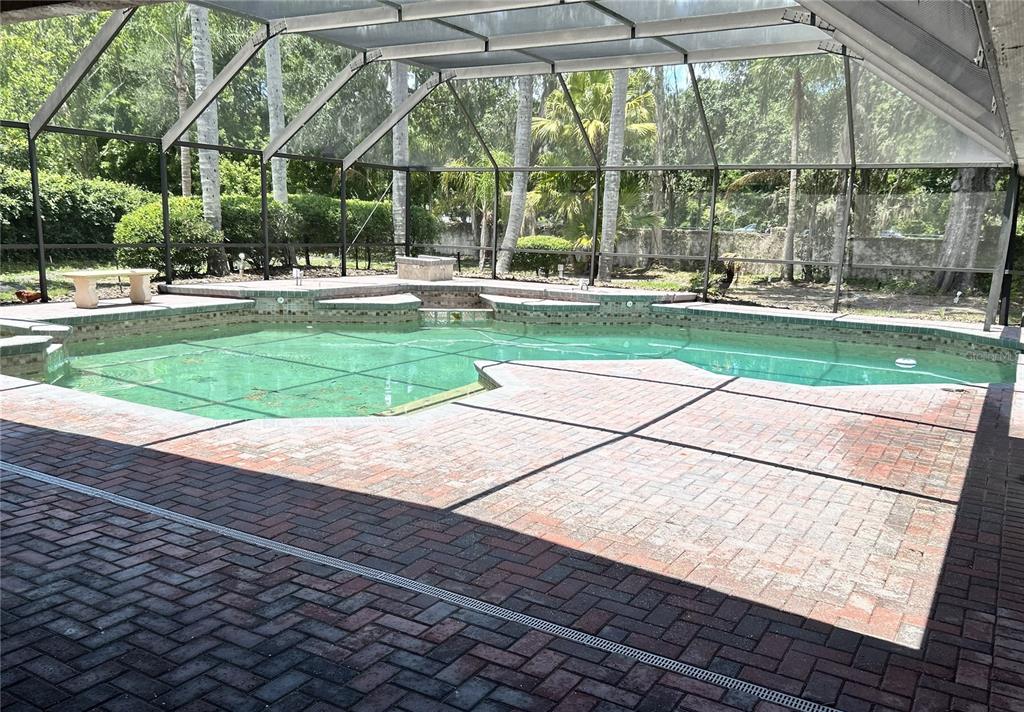 A screened-in swimming pool with a brick paver deck and a stone bench — 5106 STONEHURST ROAD, TAMPA, FL