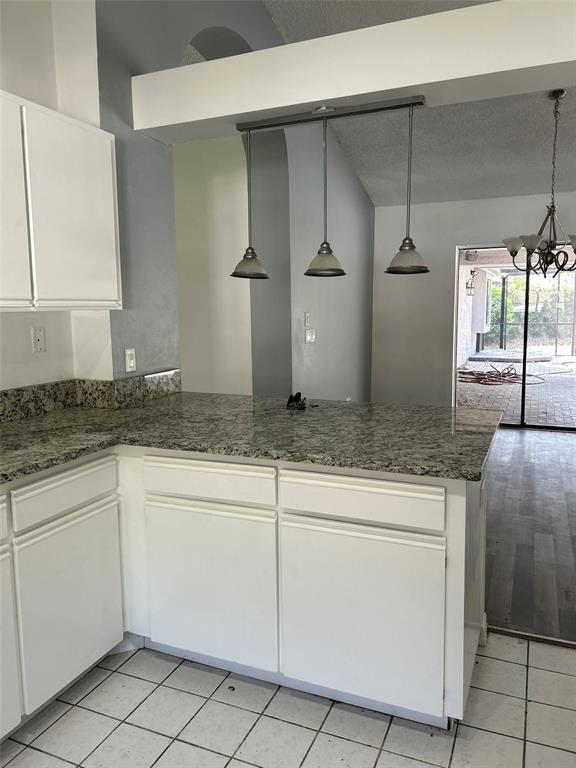 A kitchen features white cabinets, granite countertops, three pendant lights, and a tiled floor — 5106 STONEHURST ROAD, TAMPA, FL