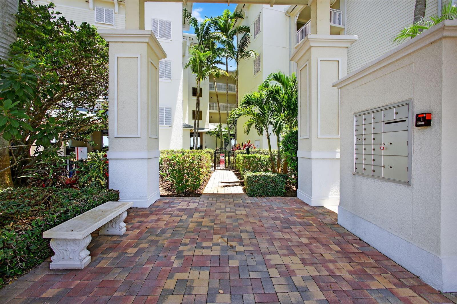 A paved walkway leads through a stone archway toward a residential building with palm trees — 275 NW Flagler Avenue # 204, Stuart FL 34994, STUART, FL