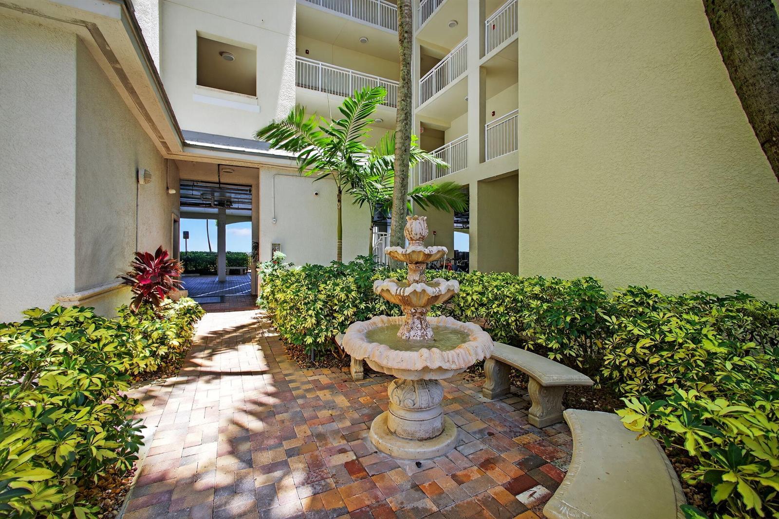 A tiered stone fountain sits in a brick courtyard surrounded by hedges and apartment balconies — 275 NW Flagler Avenue # 204, Stuart FL 34994, STUART, FL