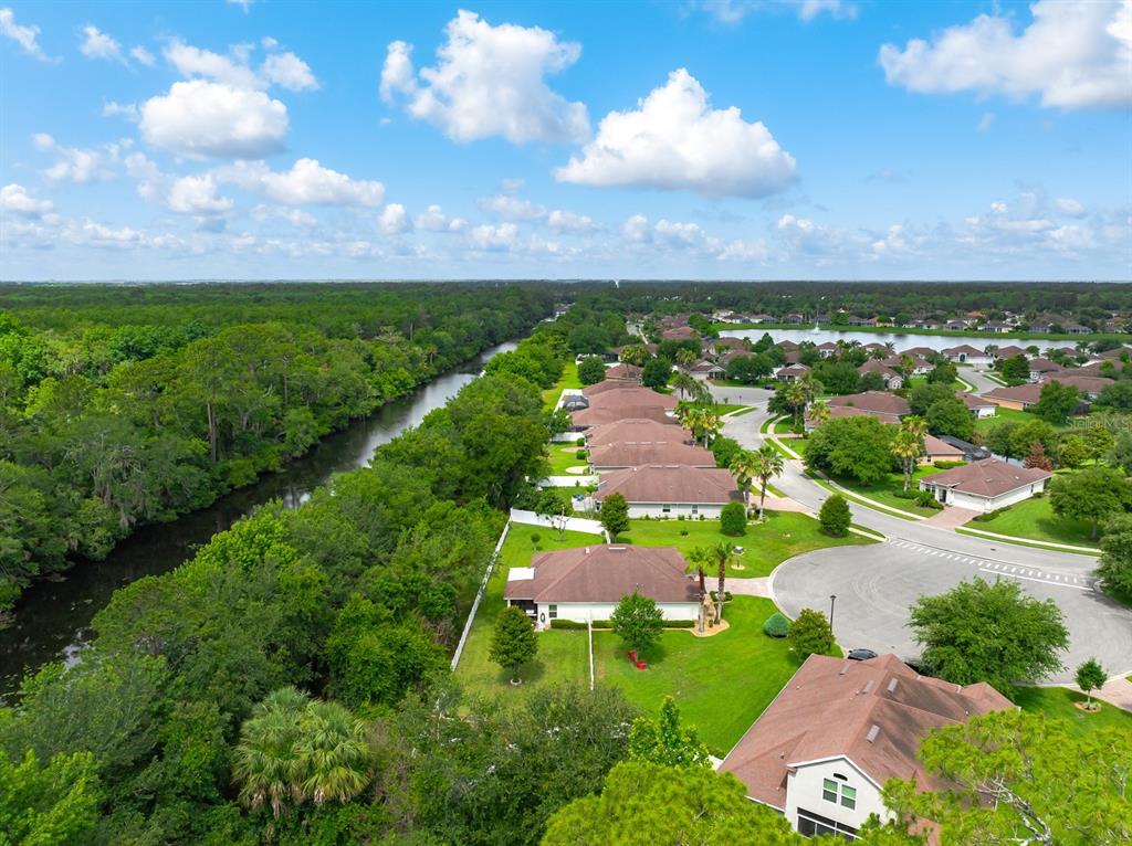 An aerial view shows a suburban neighborhood with houses bordering a wooded canal and lake — 53 AUBERRY DRIVE, PALM COAST, FL