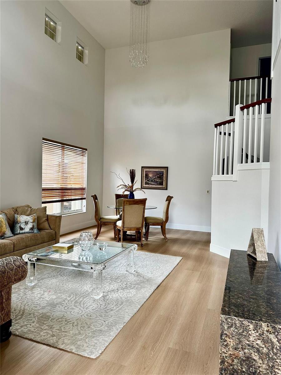 A high-ceilinged living and dining room features light wood flooring, a glass table, and stairs — 8564 Via Giardino, Boca Raton FL 33433, BOCA RATON, FL