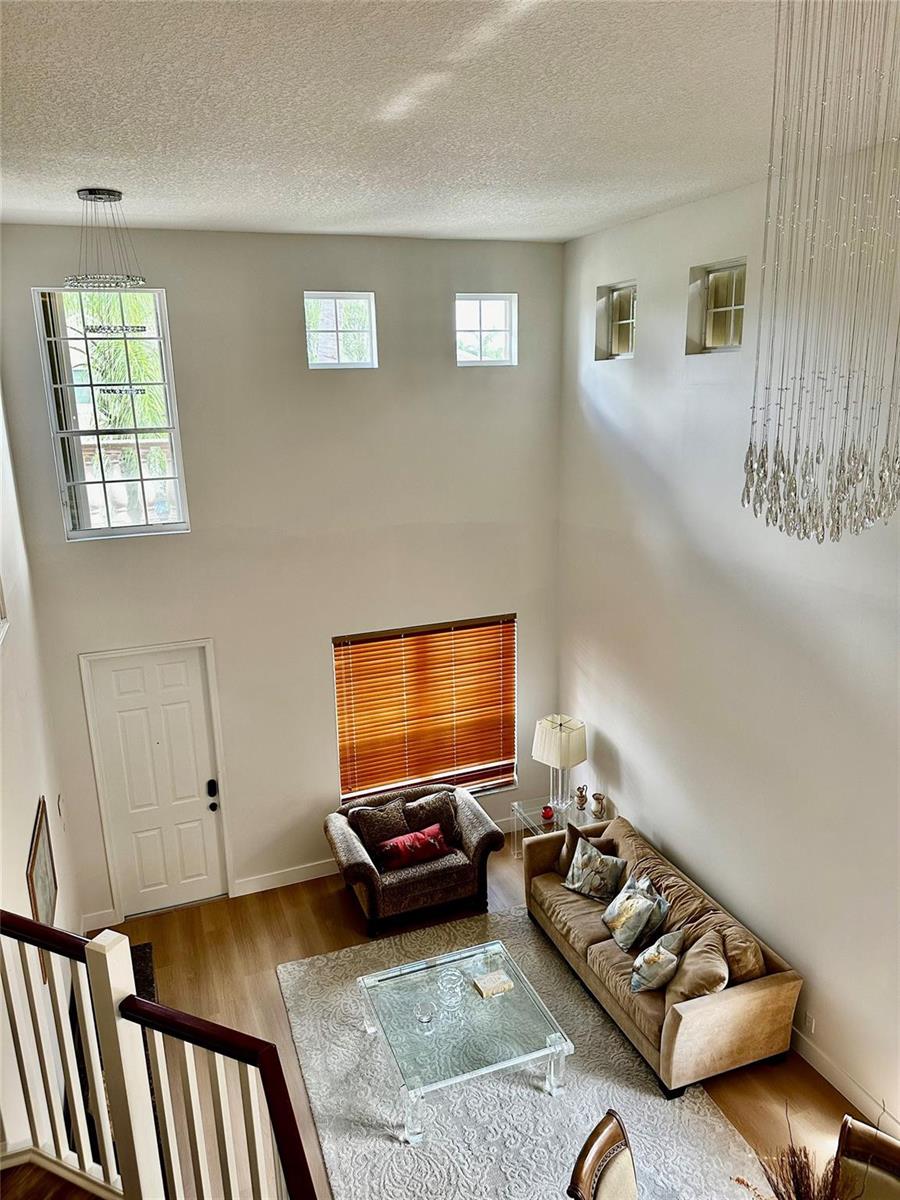 A high-ceilinged living room features a sofa, an armchair, a glass coffee table, and windows — 8564 Via Giardino, Boca Raton FL 33433, BOCA RATON, FL