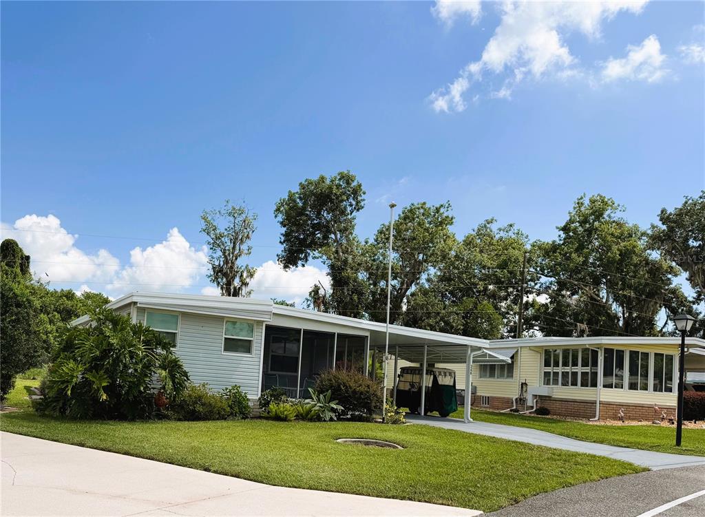 A single-story mobile home with a carport, screened porch, and green lawn under blue skies — 346 PALO VERDE DRIVE, LEESBURG, FL