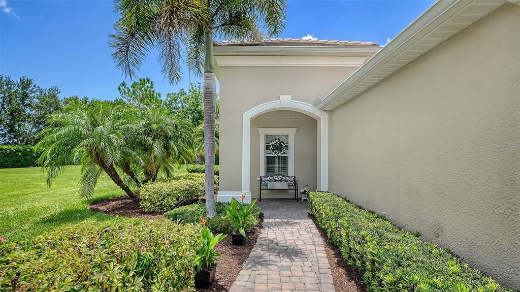 A paved walkway leads to a covered entryway with a bench and a palm tree — 4866 MAYMONT PARK CIRCLE, BRADENTON, FL