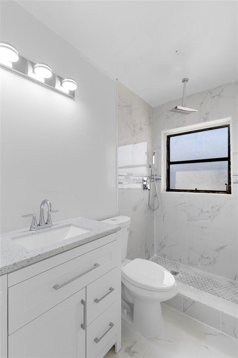 A bathroom features a white vanity, a toilet, and a walk-in shower with marble-look tile — 3313 SW 19th Street, Fort Lauderdale FL 33312, FORT LAUDERDALE, FL