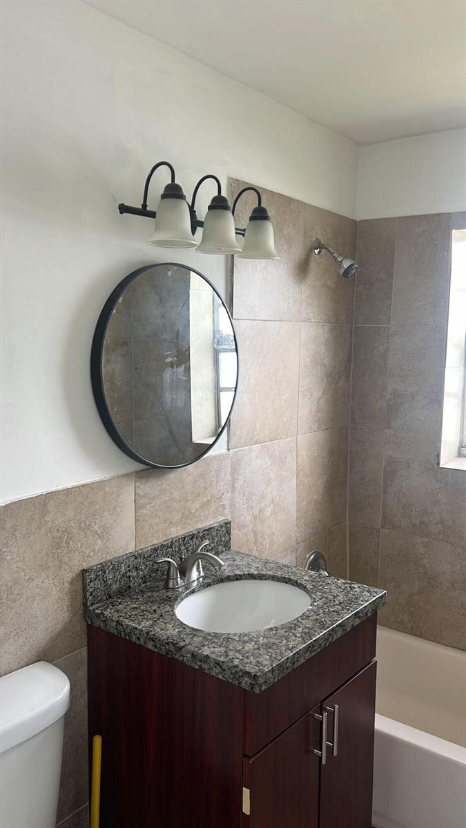 A bathroom features a dark wood vanity, granite countertop, round mirror, and tiled shower surround — 1401 N J Street # A, FL 33460, FL