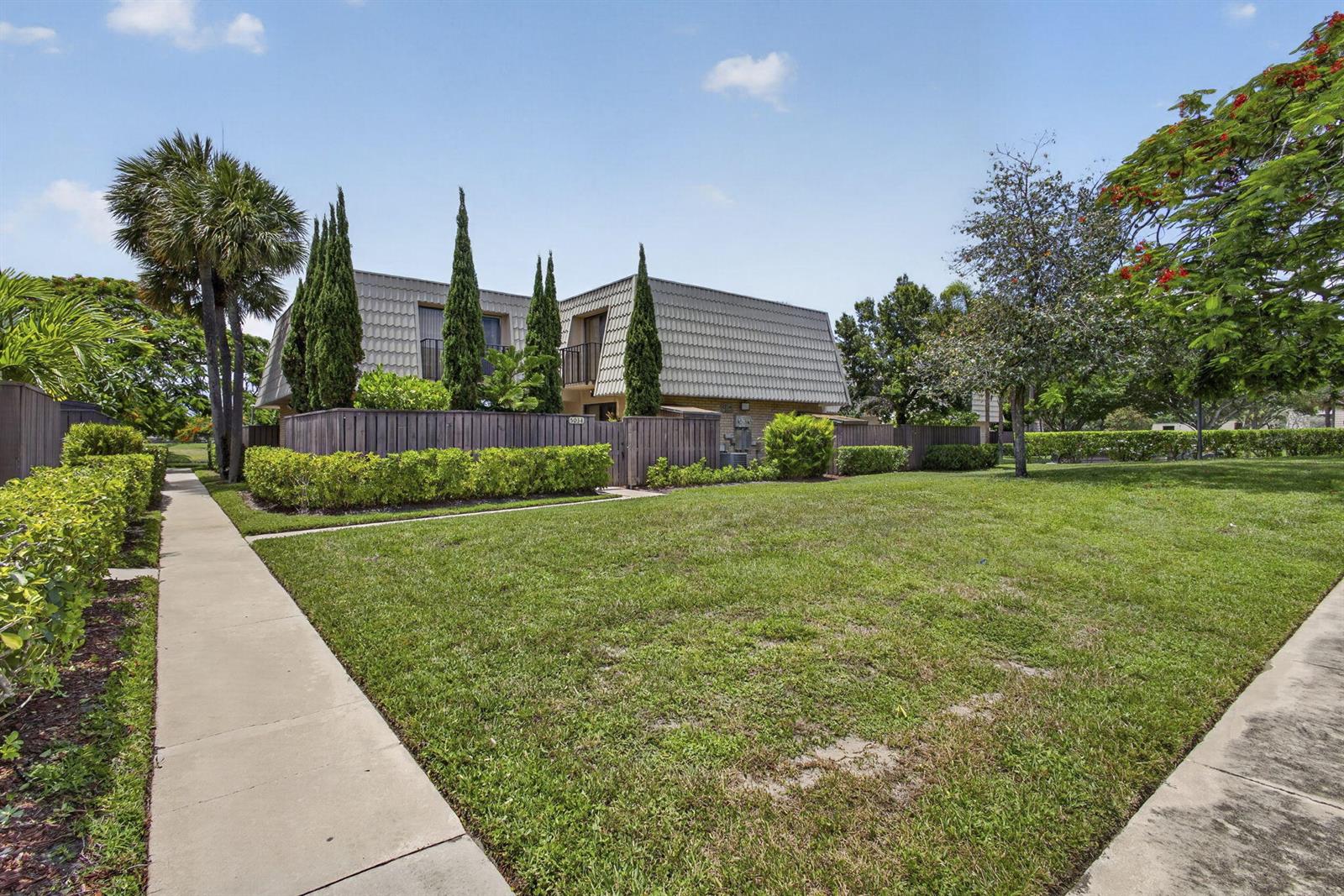 A two-story townhouse with a mansard roof sits behind a wooden fence and lawn — 5034 50th Way, West Palm Beach FL 33409, WEST PALM BEACH, FL