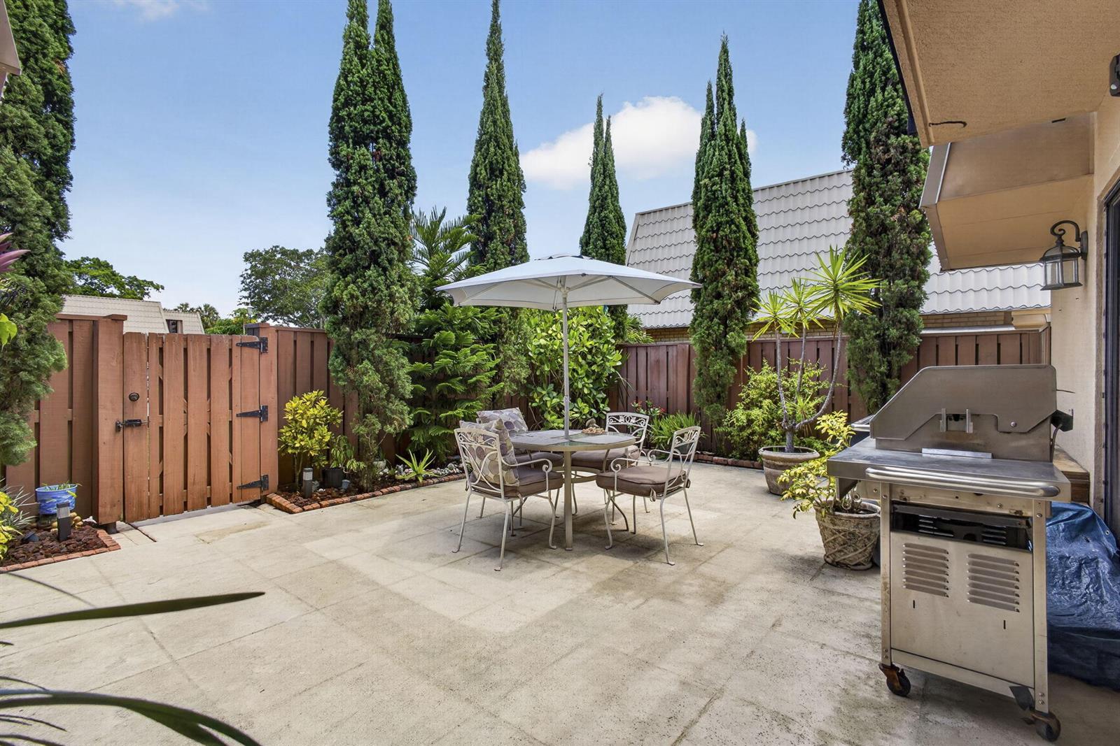 A paved backyard patio features a dining set with an umbrella and a stainless grill — 5034 50th Way, West Palm Beach FL 33409, WEST PALM BEACH, FL