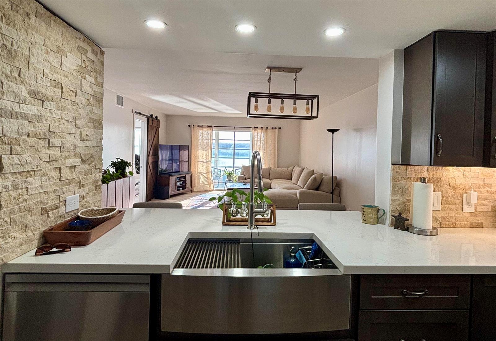 A kitchen with a stainless steel farmhouse sink overlooks an open-concept living room with views — 1501 SW 134th Way Unit 304, Pembroke Pines FL 33027, PEMBROKE PINES, FL