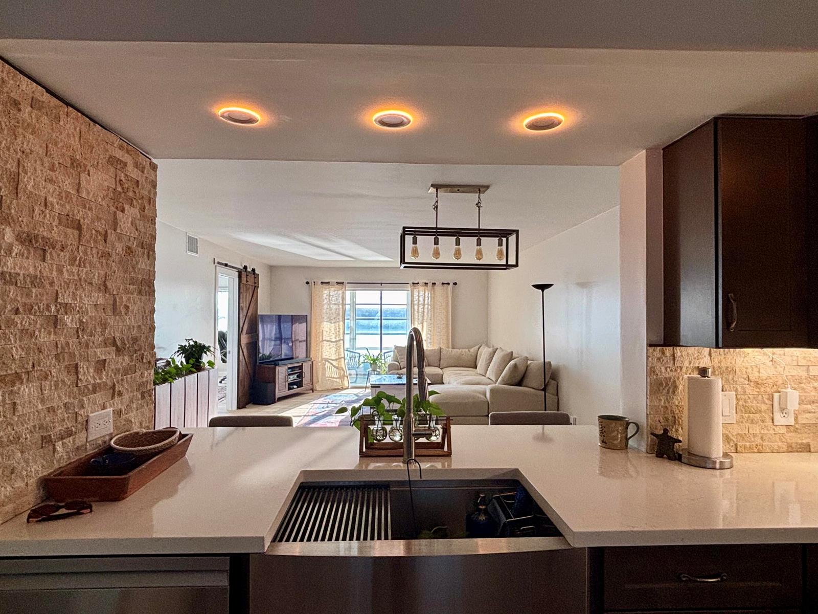 A kitchen island with a stainless steel sink overlooks a living room with a sectional sofa — 1501 SW 134th Way Unit 304, Pembroke Pines FL 33027, PEMBROKE PINES, FL