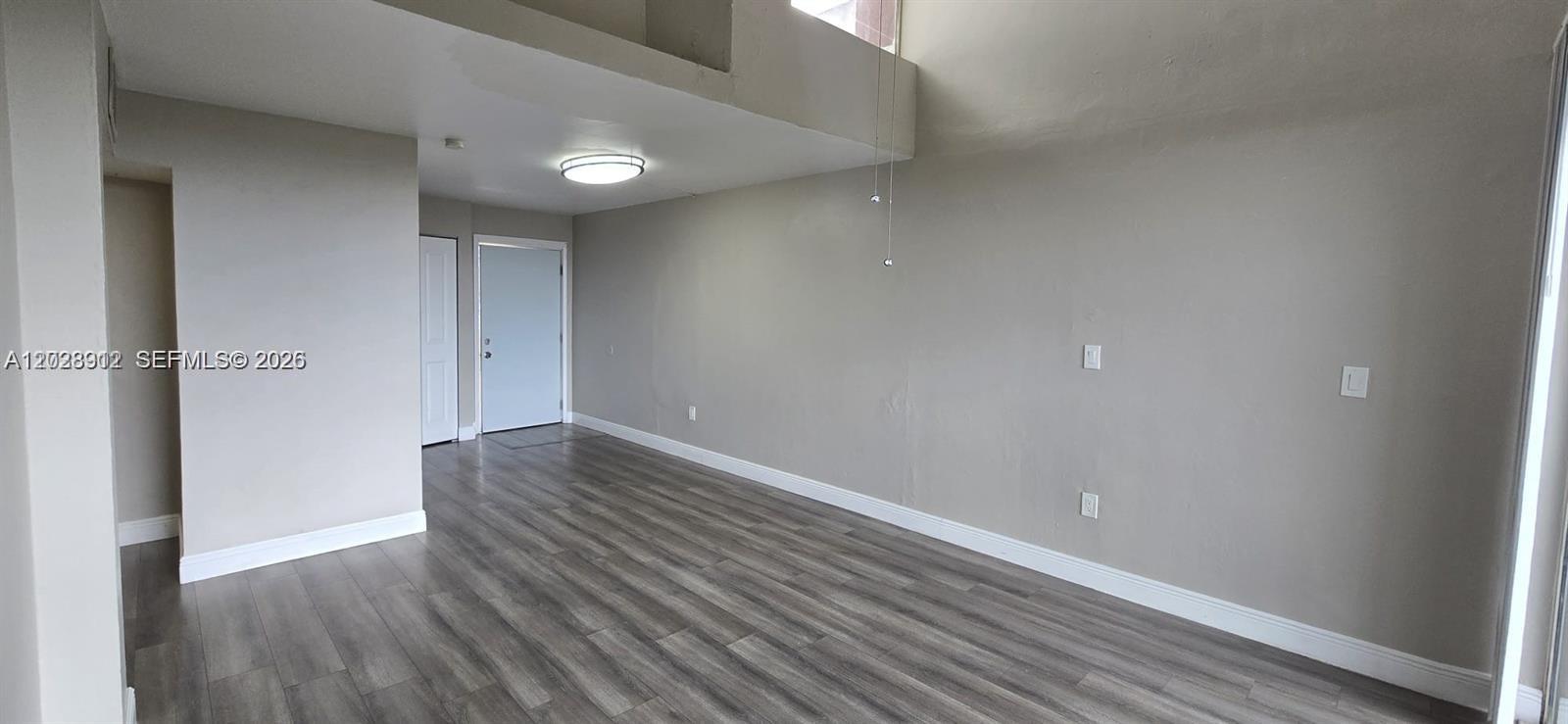 An empty room features light gray walls, dark wood-look flooring, and a white ceiling light — 8870 Fontainebleau Blvd # 502, Miami FL 33172, MIAMI, FL