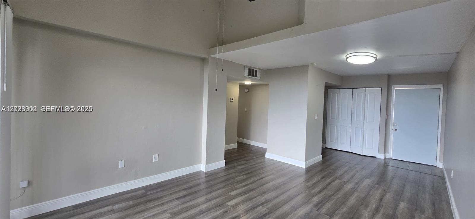 An empty room features light gray walls, dark wood-look flooring, and a white entry door — 8870 Fontainebleau Blvd # 502, Miami FL 33172, MIAMI, FL