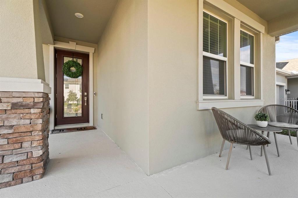 A covered front porch features a brown door, stone accents, and two outdoor chairs — 11632 PARAGRAPH ROAD, ORLANDO, FL