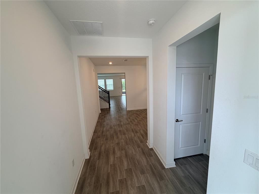 A hallway with wood-look tile flooring leads to an open living area with a staircase — 11632 PARAGRAPH ROAD, ORLANDO, FL