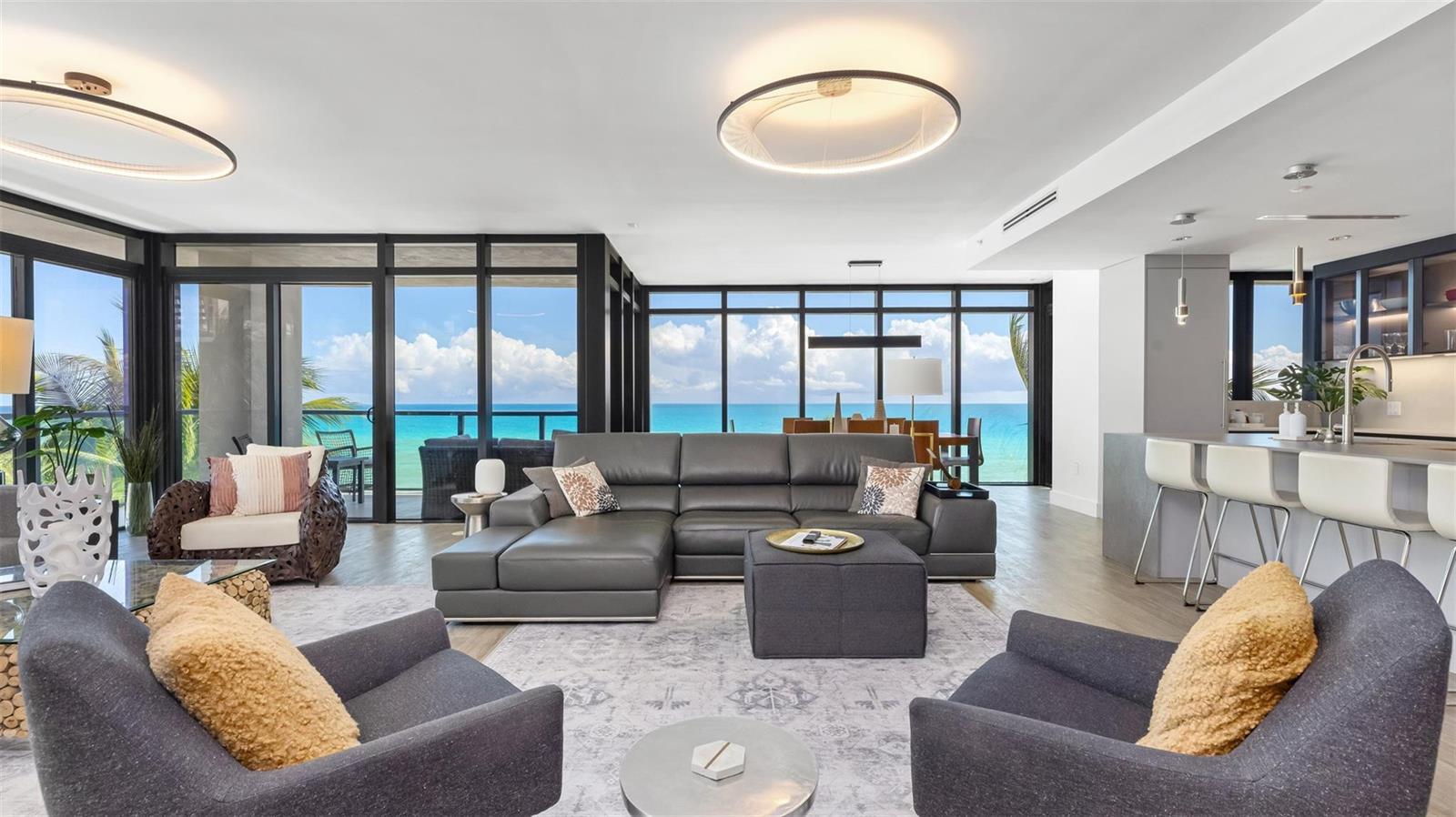 A modern living room features a grey sectional, two armchairs, and floor-to-ceiling ocean views — 2205 S Surf Road # 4b, Hollywood FL 33019, HOLLYWOOD, FL