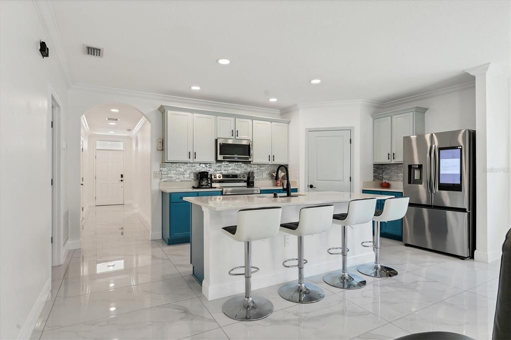 A modern kitchen features a white island with bar stools, blue cabinets, and stainless appliances — 177 TIERRA VERDE WAY, BRADENTON, FL