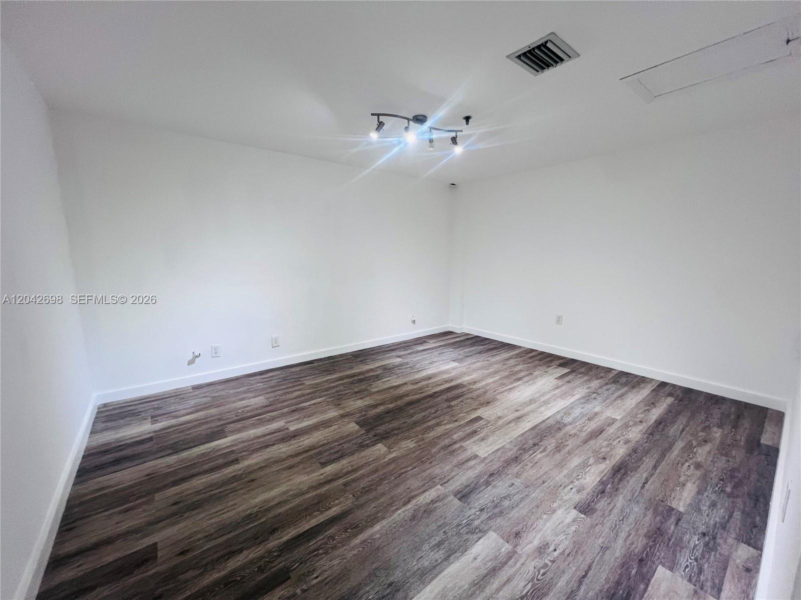 An empty room features white walls, dark wood-look flooring, and a track lighting fixture — 7500 NW 25th St # 256, Miami FL 33122, MIAMI, FL