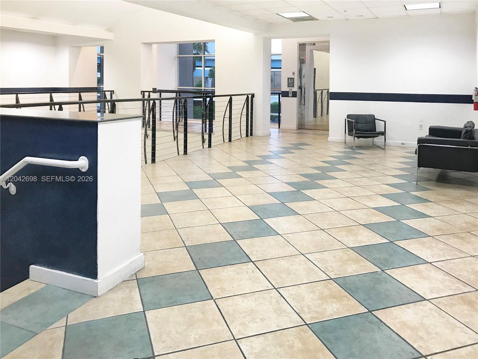 A bright lobby features a checkered tile floor, a blue accent wall, and metal railings — 7500 NW 25th St # 256, Miami FL 33122, MIAMI, FL