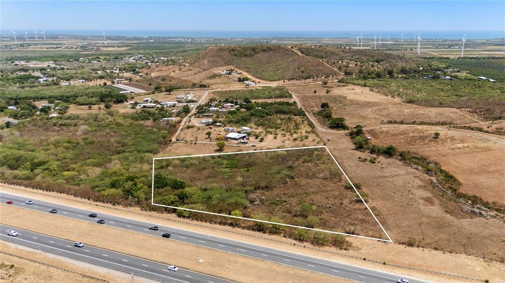 An aerial view shows a vacant, trapezoidal plot of land adjacent to a multi-lane highway — BO. DESCALABRADO, SANTA ISABEL, PR