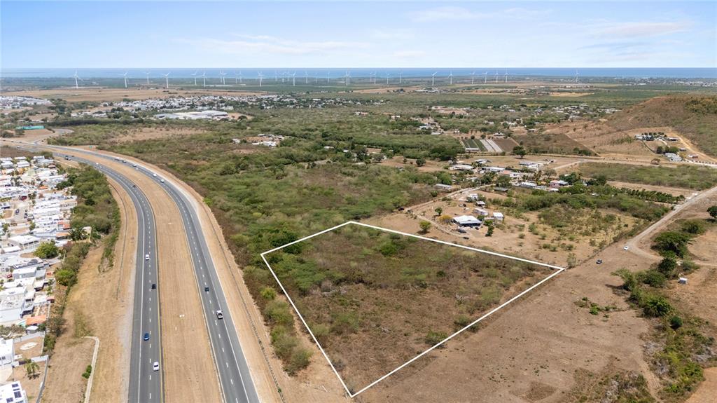 An aerial view shows a vacant, trapezoidal plot of land adjacent to a multi-lane highway — BO. DESCALABRADO, SANTA ISABEL, PR