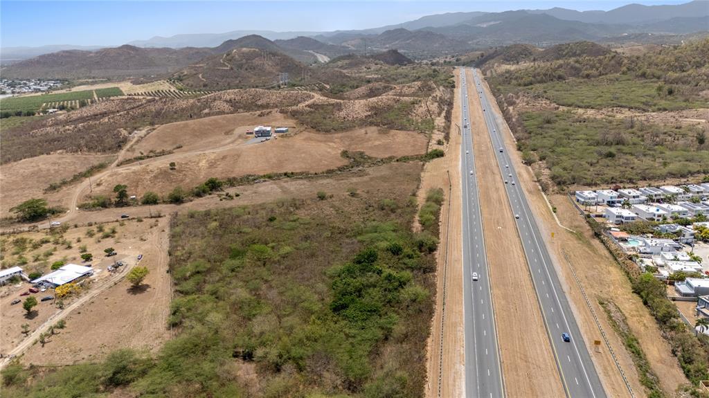 An aerial view shows a multi-lane highway running alongside undeveloped land and residential properties — BO. DESCALABRADO, SANTA ISABEL, PR