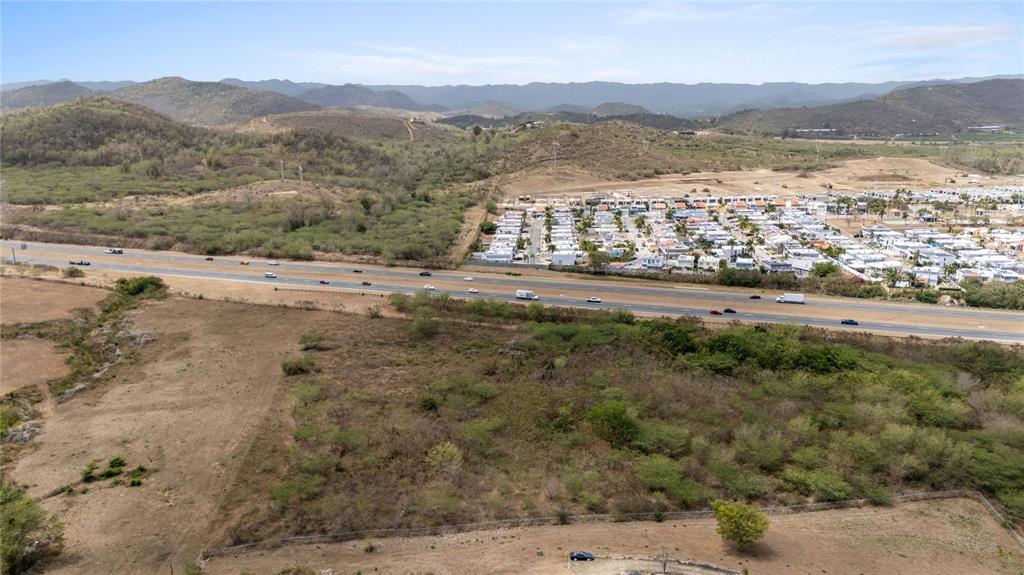 An aerial view shows a highway separating a rural field from a residential neighborhood — BO. DESCALABRADO, SANTA ISABEL, PR