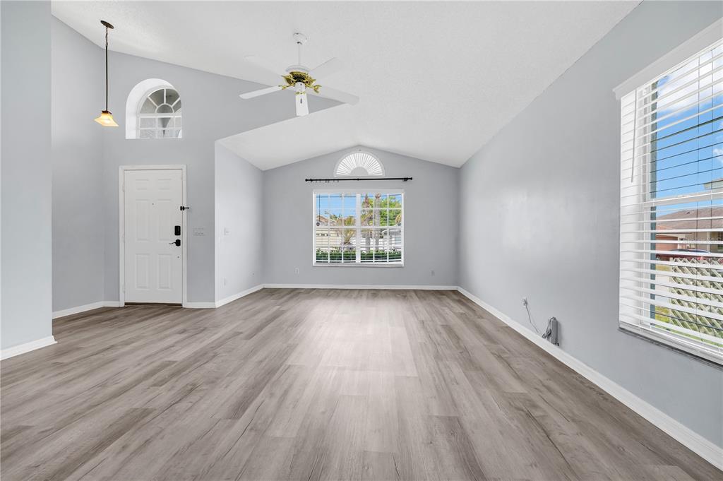 An empty living room features light gray walls, wood-look flooring, a vaulted ceiling, and windows — 515 LAKE DAVENPORT BOULEVARD, DAVENPORT, FL