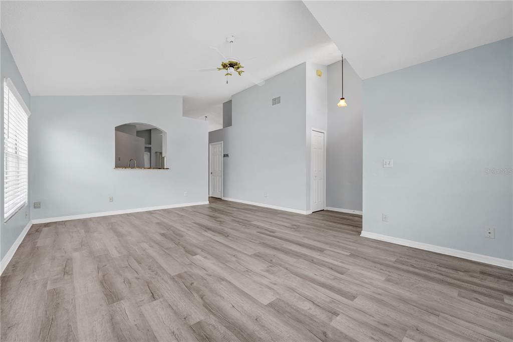 An empty living room features light gray walls, vaulted ceilings, and wood-look vinyl plank flooring — 515 LAKE DAVENPORT BOULEVARD, DAVENPORT, FL