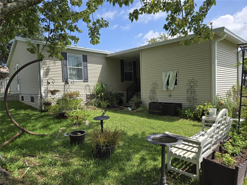 A beige vinyl-sided house features a grassy yard with a bench and garden decor — 2723 LAKE GRASSMERE CIRCLE UNIT 910, ZELLWOOD, FL