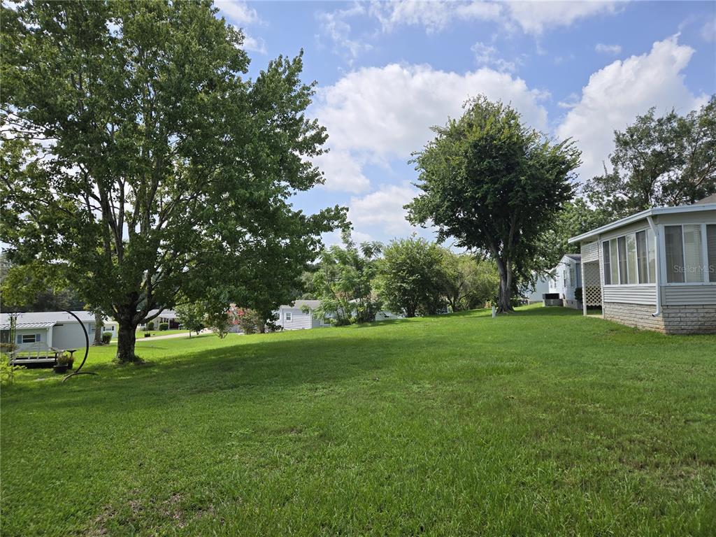 A grassy backyard features large shade trees and a side view of a mobile home — 2723 LAKE GRASSMERE CIRCLE UNIT 910, ZELLWOOD, FL