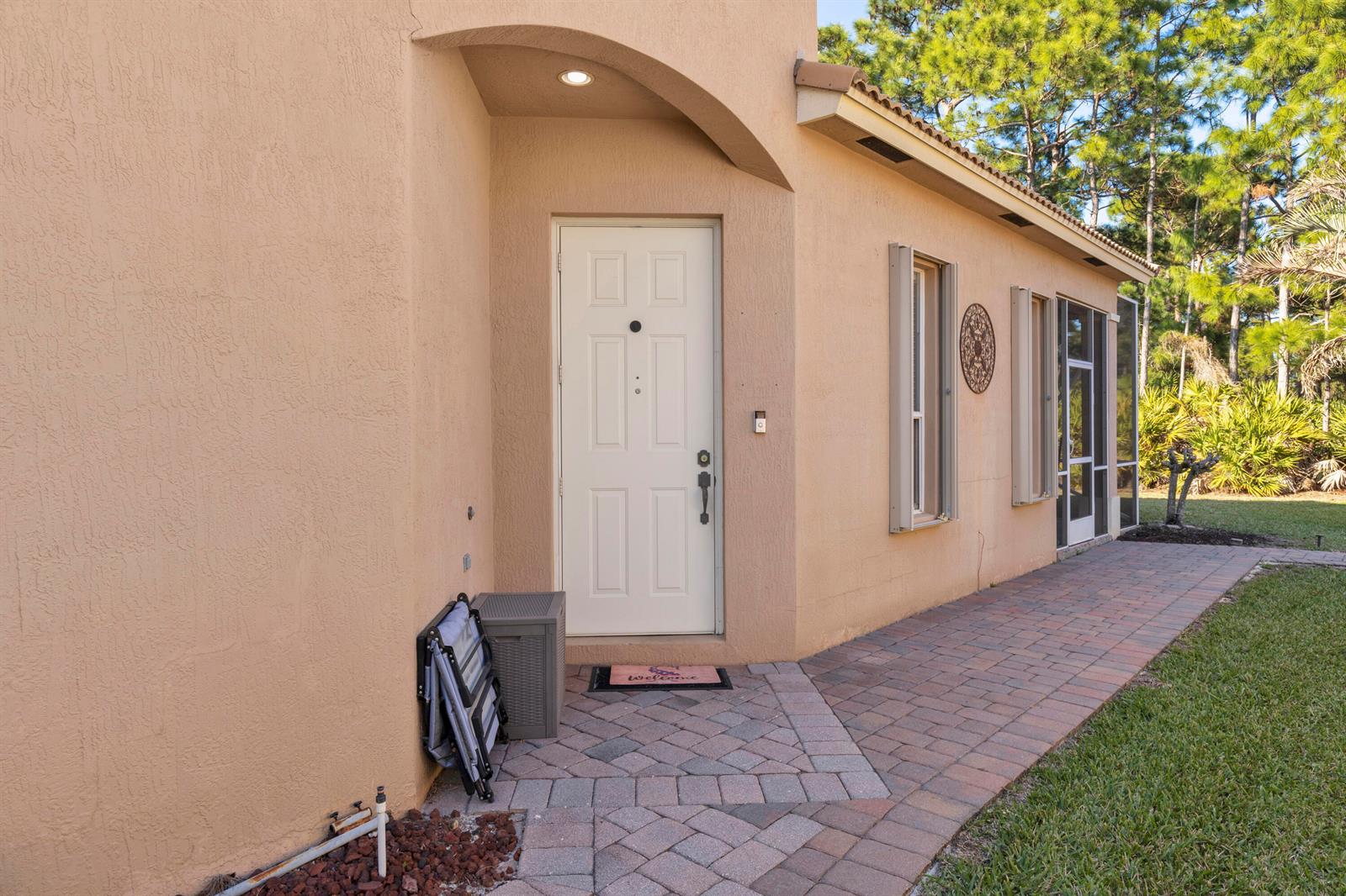 An exterior view of a tan stucco house with a white front door and brick walkway — 5726 Sterling Lake Drive, Fort Pierce FL 34951, FORT PIERCE, FL