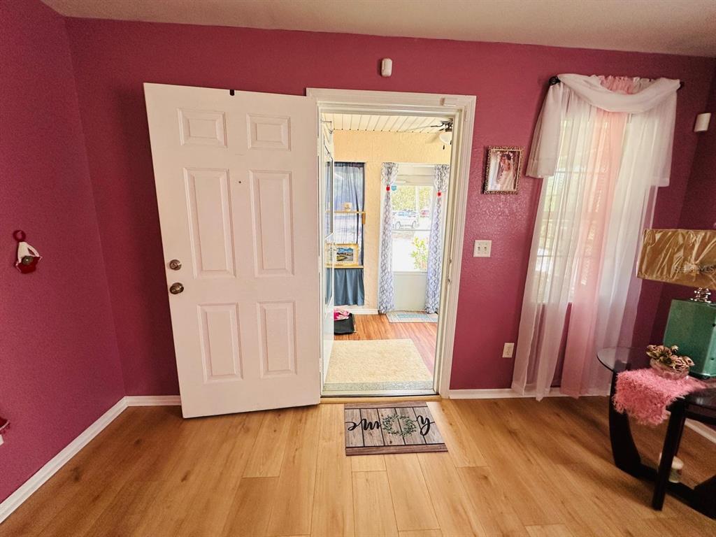 A room with magenta walls, wood-look flooring, and an open door leading to a porch — 224 MONTEGO DRIVE, SEBRING, FL