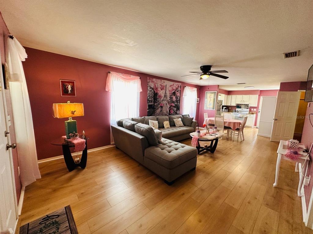 A living room with light wood floors, a gray sectional sofa, and a dining area — 224 MONTEGO DRIVE, SEBRING, FL