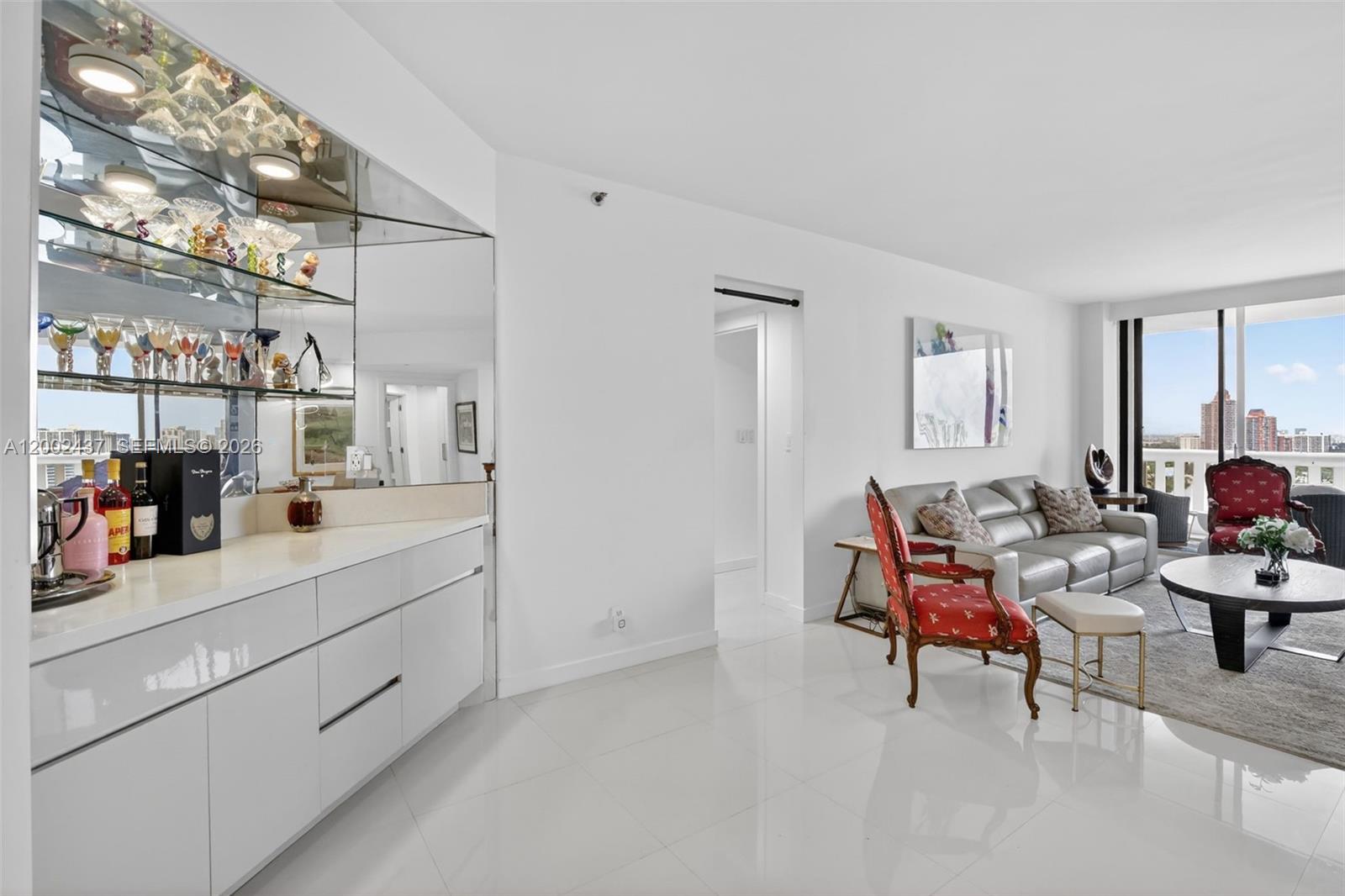 A modern living room features a white wet bar with mirrored shelving and balcony views — 3000 Island Blvd # 2404, Aventura FL 33160, AVENTURA, FL