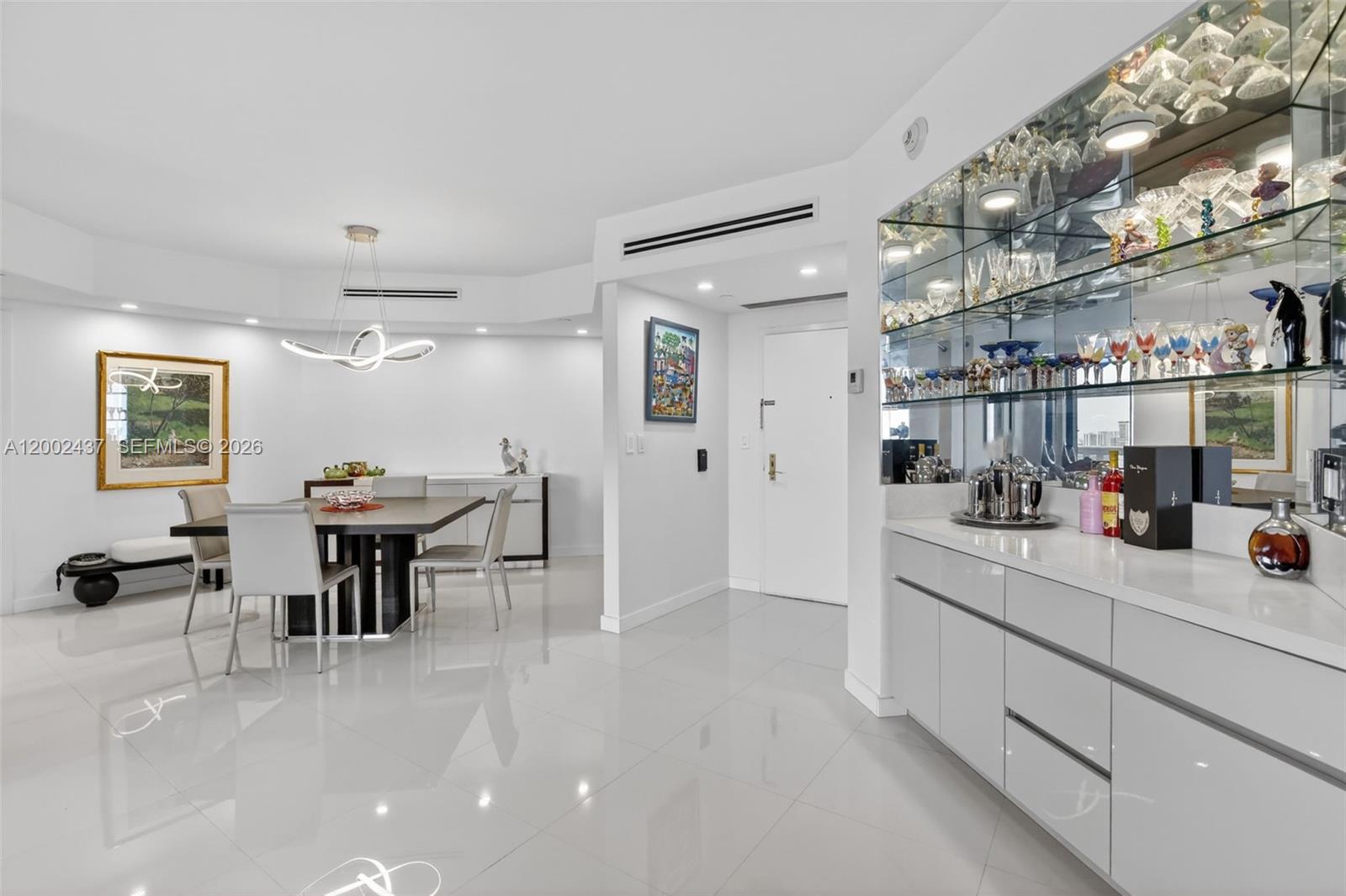 A dining area with a modern chandelier and a mirrored bar with glass shelving — 3000 Island Blvd # 2404, Aventura FL 33160, AVENTURA, FL
