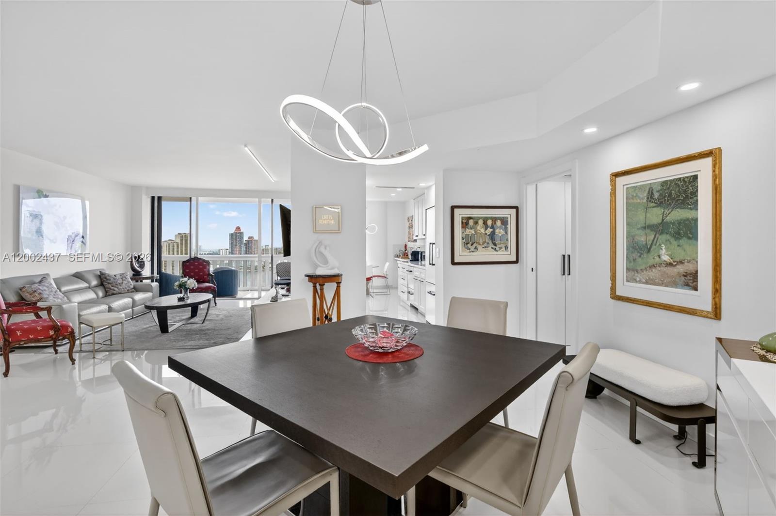 A dining area with a square table and modern chandelier opens into a bright living room — 3000 Island Blvd # 2404, Aventura FL 33160, AVENTURA, FL